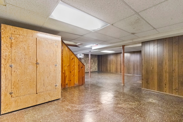 basement with a paneled ceiling and wood walls