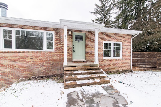 snow covered property entrance featuring brick siding and fence