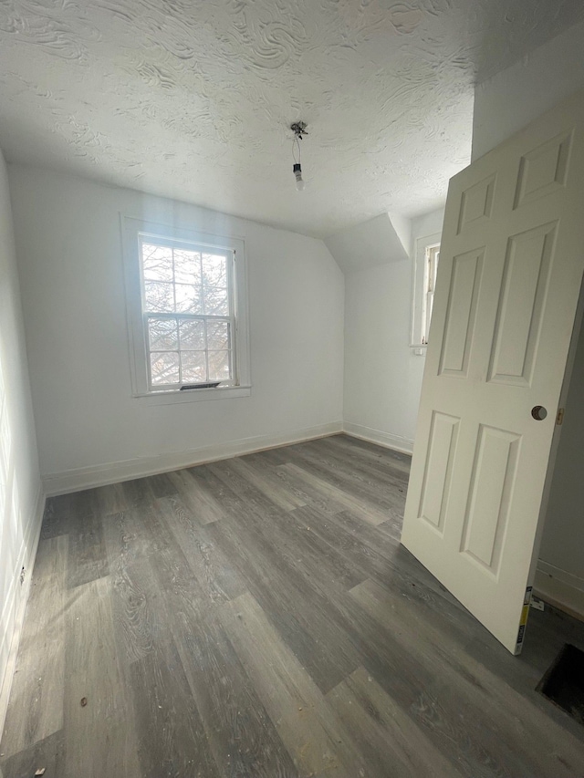bonus room with baseboards, a textured ceiling, and wood finished floors