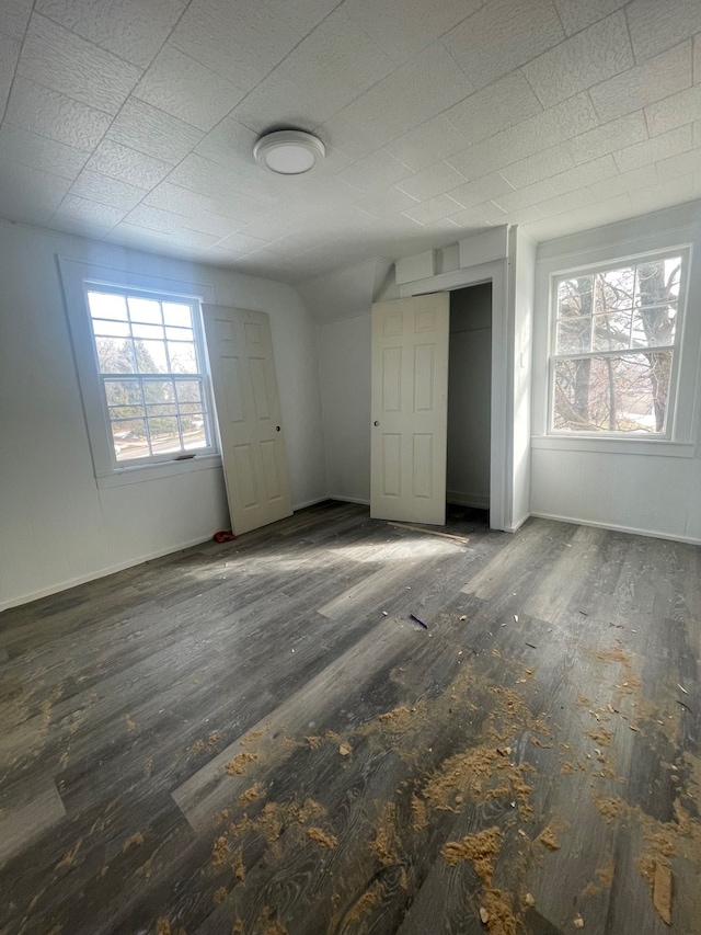 unfurnished bedroom with vaulted ceiling, baseboards, a closet, and wood finished floors