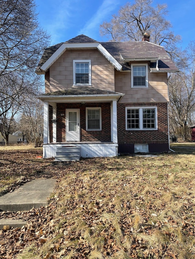view of front facade featuring a shingled roof, a chimney, a porch, and brick siding