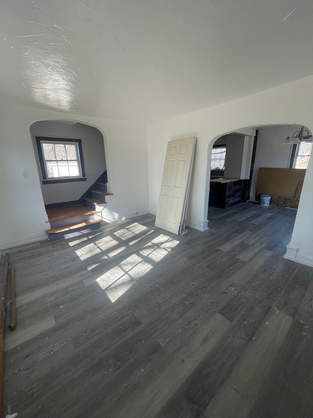 unfurnished living room featuring arched walkways, baseboards, and wood finished floors