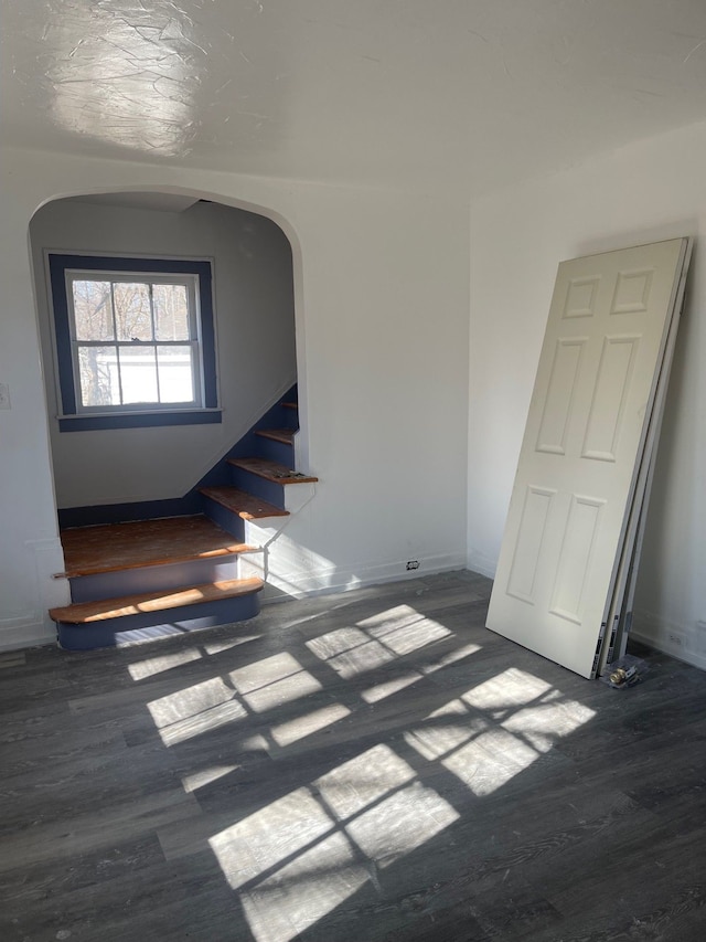 unfurnished room featuring arched walkways, baseboards, stairs, and wood finished floors
