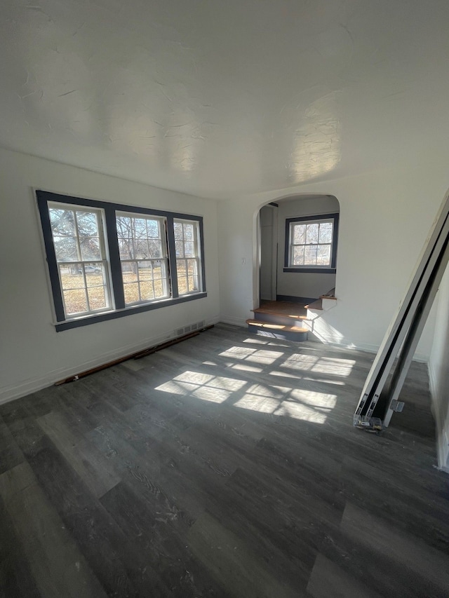 unfurnished living room featuring arched walkways and wood finished floors