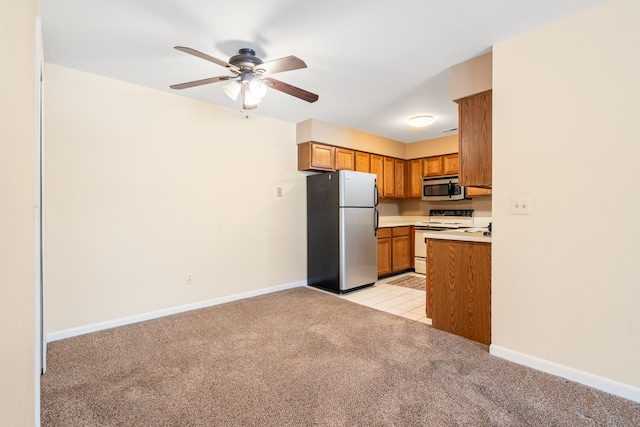 kitchen featuring brown cabinetry, ceiling fan, light carpet, light countertops, and appliances with stainless steel finishes
