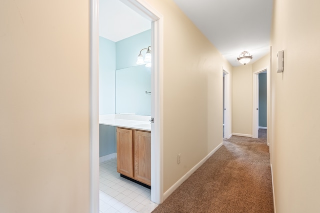hallway with light colored carpet, baseboards, and light tile patterned flooring