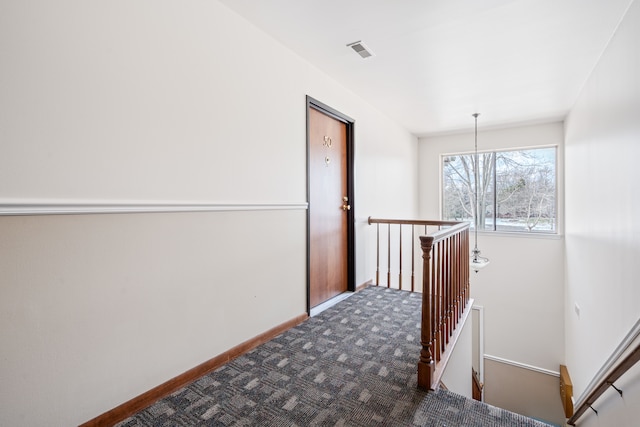 corridor featuring baseboards, dark colored carpet, visible vents, and an upstairs landing