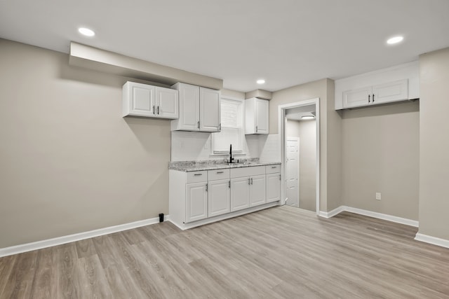 kitchen featuring light stone countertops, light wood-type flooring, decorative backsplash, and white cabinets