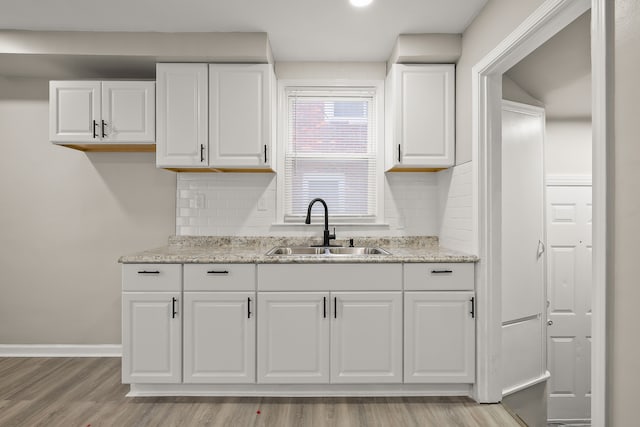 kitchen featuring light wood-type flooring, light stone countertops, sink, and white cabinets