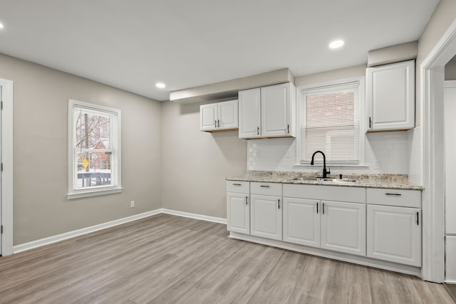 kitchen featuring sink, white cabinetry, light stone counters, light hardwood / wood-style floors, and decorative backsplash