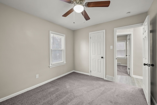 unfurnished bedroom with multiple windows, light colored carpet, and ceiling fan