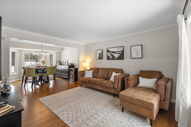 living room featuring wood-type flooring, ornamental molding, and a notable chandelier