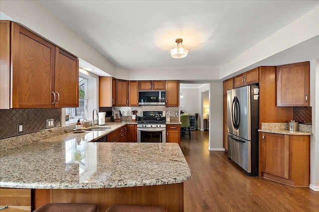 kitchen with sink, a breakfast bar area, stainless steel appliances, light stone countertops, and kitchen peninsula