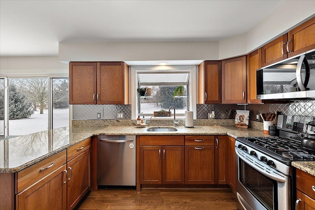 kitchen featuring appliances with stainless steel finishes, sink, backsplash, light stone countertops, and dark wood-type flooring