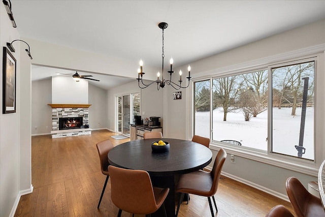 dining area featuring a stone fireplace, vaulted ceiling, light hardwood / wood-style floors, and ceiling fan with notable chandelier