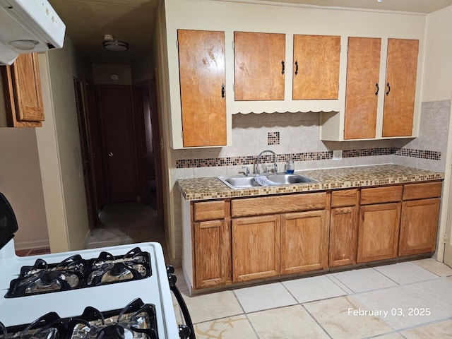 kitchen with light tile patterned flooring, sink, range with gas cooktop, and backsplash