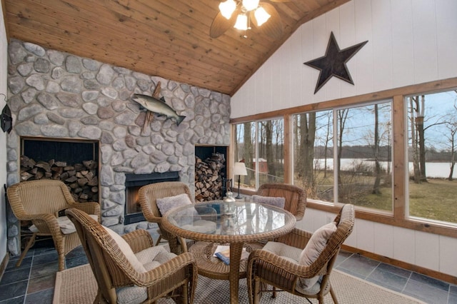 sunroom featuring ceiling fan, lofted ceiling, a stone fireplace, and wooden ceiling