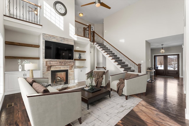 living room with dark wood-type flooring, a towering ceiling, a fireplace, and ceiling fan