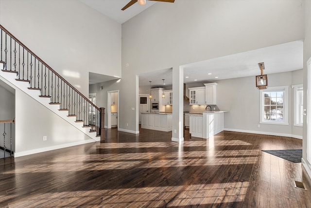 unfurnished living room with dark hardwood / wood-style flooring, sink, a towering ceiling, and ceiling fan