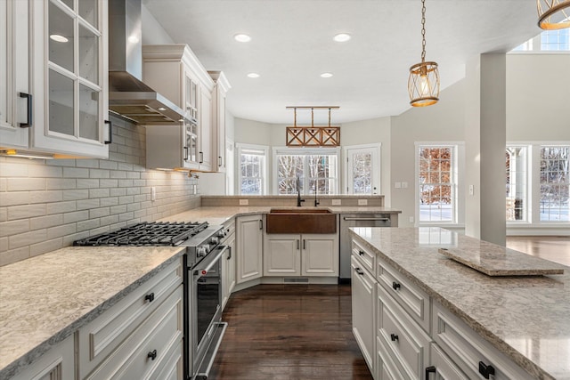 kitchen with sink, appliances with stainless steel finishes, pendant lighting, wall chimney range hood, and white cabinets