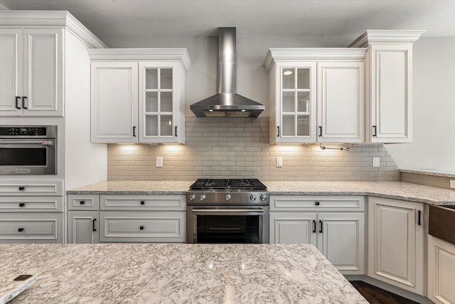 kitchen featuring white cabinets, backsplash, wall chimney exhaust hood, and appliances with stainless steel finishes