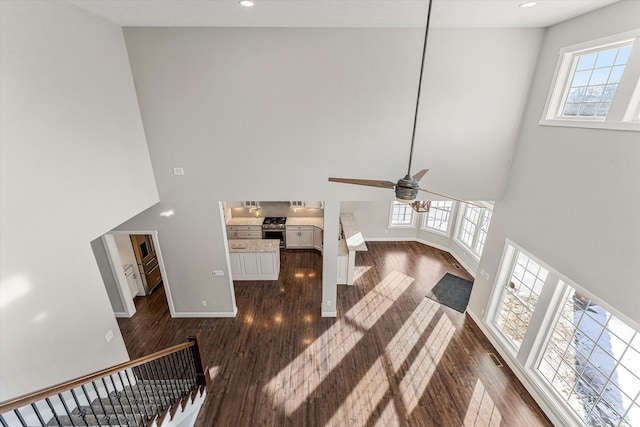 living room with dark wood-type flooring, ceiling fan, and a high ceiling