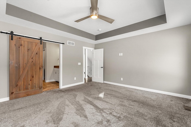 unfurnished bedroom featuring connected bathroom, carpet floors, a barn door, and a raised ceiling