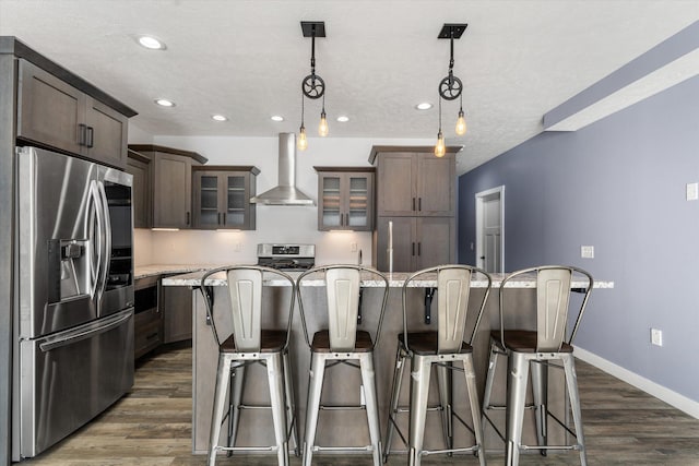 kitchen featuring a kitchen island, appliances with stainless steel finishes, wall chimney range hood, and hanging light fixtures