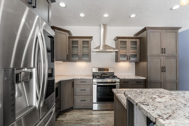 kitchen featuring light stone counters, dark wood-type flooring, wall chimney exhaust hood, and appliances with stainless steel finishes