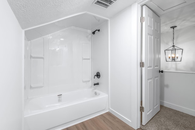 bathroom with hardwood / wood-style floors, a textured ceiling, and washtub / shower combination