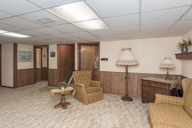 living area with a paneled ceiling, light carpet, and wood walls