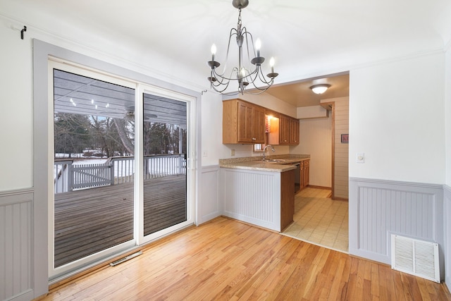 kitchen featuring pendant lighting, sink, kitchen peninsula, an inviting chandelier, and light hardwood / wood-style flooring