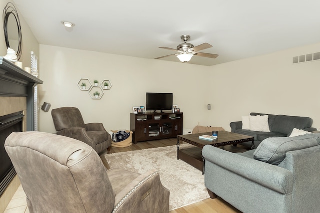 living room with ceiling fan, a tile fireplace, and light wood-type flooring