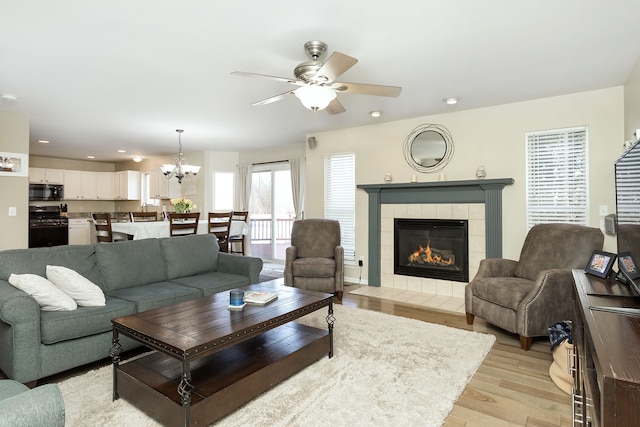 living room featuring ceiling fan with notable chandelier, a fireplace, and light hardwood / wood-style floors