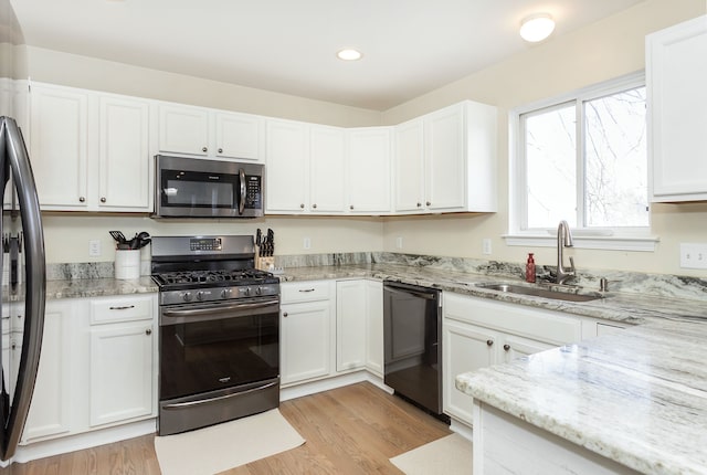 kitchen with stainless steel appliances, light stone countertops, sink, and white cabinets