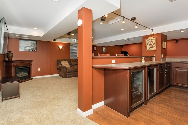 bar featuring dark brown cabinets, track lighting, beverage cooler, and light wood-type flooring