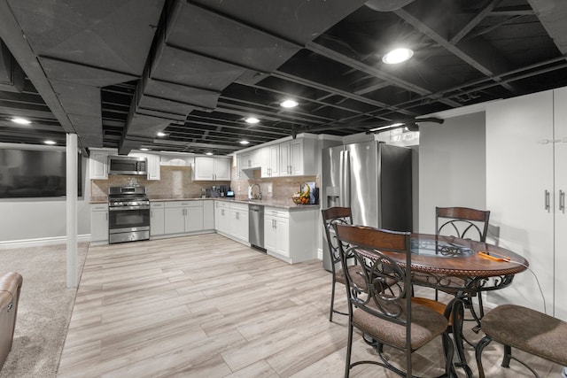 kitchen with appliances with stainless steel finishes, tasteful backsplash, white cabinetry, sink, and light wood-type flooring