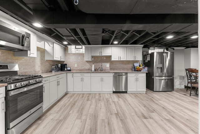 kitchen with appliances with stainless steel finishes, backsplash, white cabinets, and light hardwood / wood-style floors