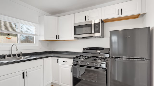 kitchen featuring stainless steel appliances, dark countertops, a sink, and white cabinetry