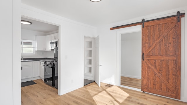 kitchen featuring a barn door, white cabinets, dark countertops, light wood-style flooring, and black range with gas stovetop