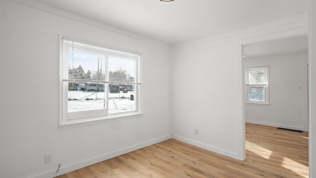 spare room with light wood-type flooring, visible vents, and baseboards