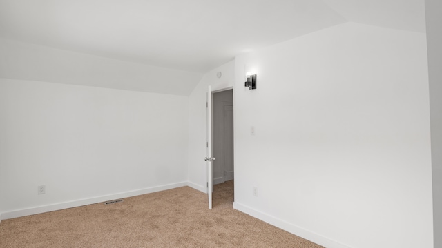 empty room with baseboards, visible vents, vaulted ceiling, and light colored carpet