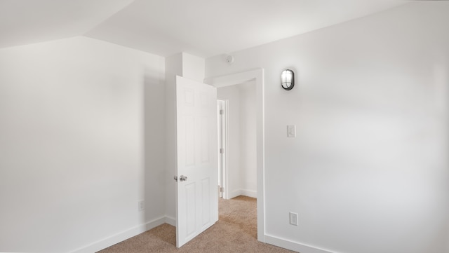 unfurnished bedroom with baseboards, vaulted ceiling, and light colored carpet