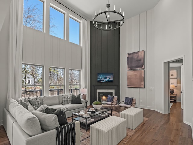 living area featuring wood finished floors, a towering ceiling, a large fireplace, baseboards, and a chandelier