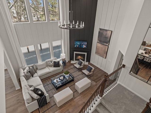 living area featuring an inviting chandelier, a large fireplace, a high ceiling, and wood finished floors
