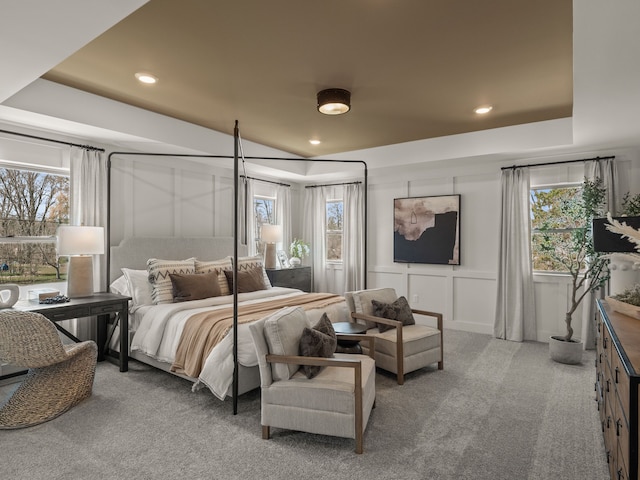 bedroom with a tray ceiling, carpet floors, multiple windows, and a decorative wall