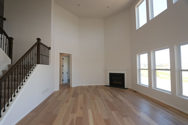 unfurnished living room featuring a high ceiling, visible vents, a healthy amount of sunlight, and light wood-style flooring