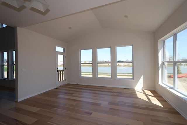 empty room featuring a water view, baseboards, wood finished floors, and lofted ceiling