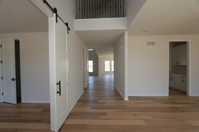 hallway featuring visible vents, a barn door, baseboards, and light wood-type flooring