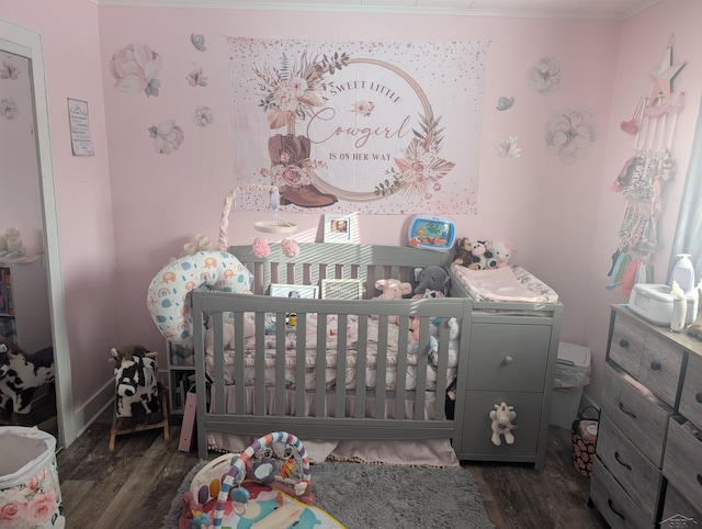 bedroom featuring dark wood-type flooring, ornamental molding, and a nursery area